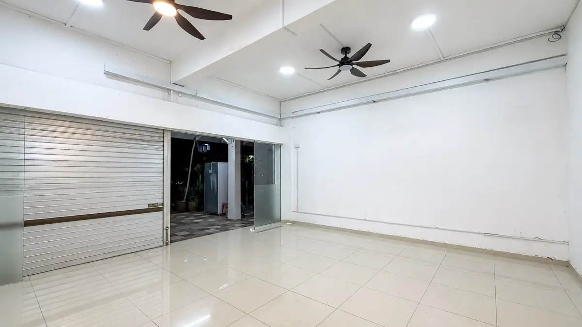 An empty storefront interior with a closed metal roll-up door and glass entry on the left, glossy tiled floor, white walls, and ceiling fans overhead.