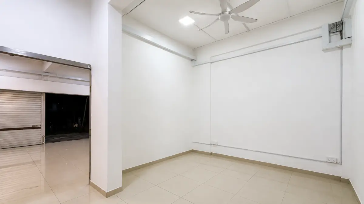 Empty white room with tiled floor and ceiling fan; open shop shutter reveals nighttime street outside (interior of a storefront).