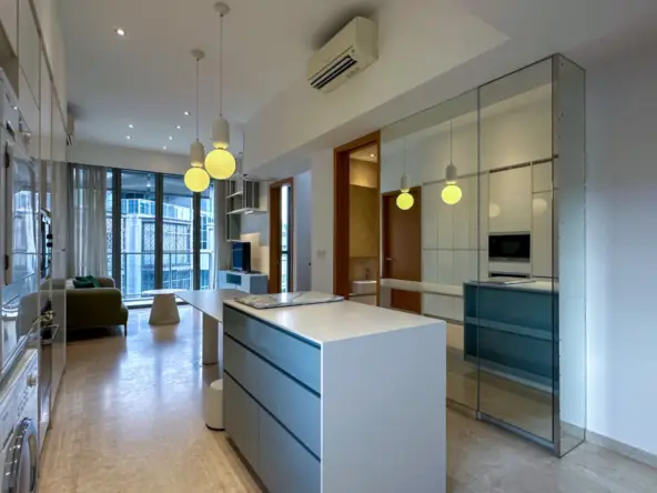 Open-concept kitchen with a white island, blue-drawer cabinets, and three hanging pendant lights leading to a living area with floor-to-ceiling windows.
