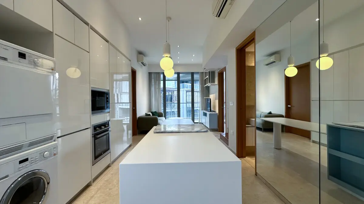 Modern open-concept kitchen with a white island, glossy cabinetry, and built-in appliances leading to a living area.