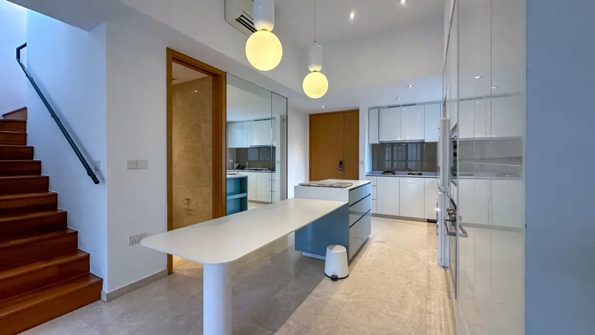 Open-plan kitchen with white cabinets, a blue island, and a white dining table; wooden stairs along the left wall.