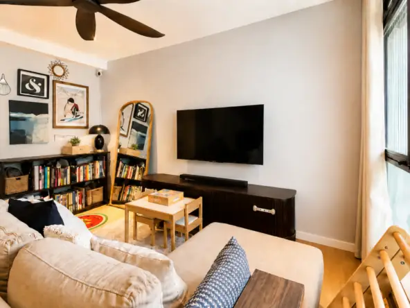 Cozy living room with a beige sectional, wall-mounted TV, and a dark media console beside a large windowed wall.