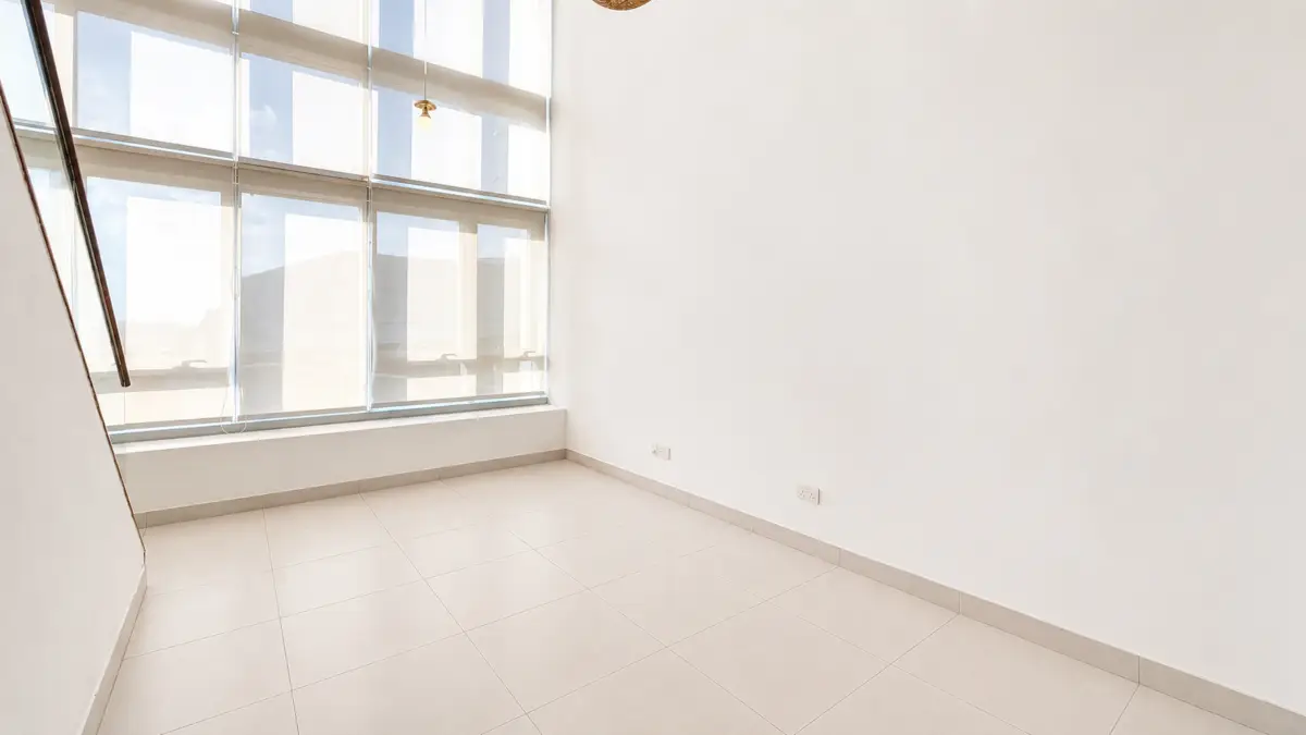 Bright empty corner of a modern room with large floor-to-ceiling windows along one wall, beige tiled floor, and white walls.