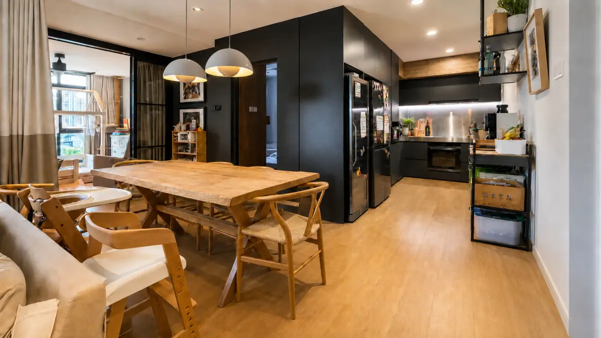 Open-plan kitchen and dining area with a large wooden table, matching chairs, and black modern cabinets.