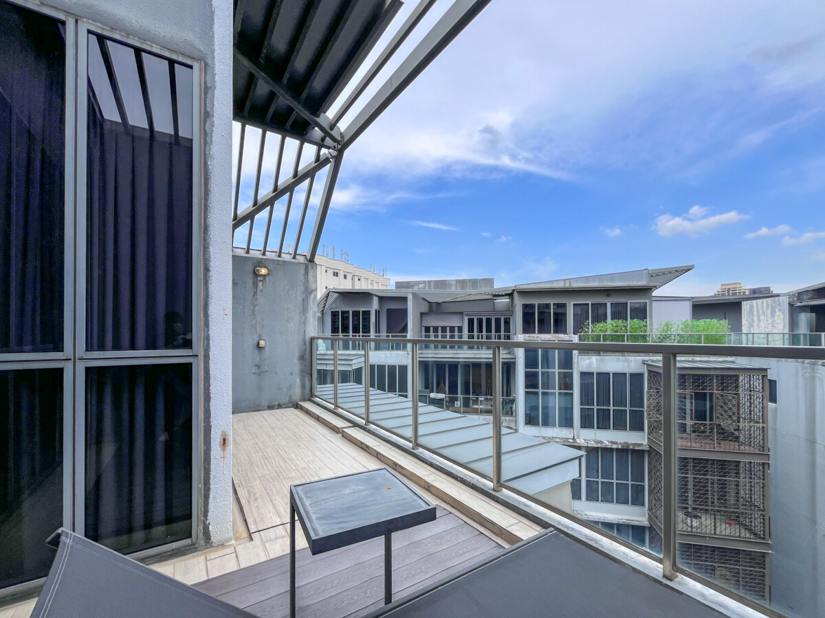 Balcony with glass railing overlooking modern buildings and a blue sky.