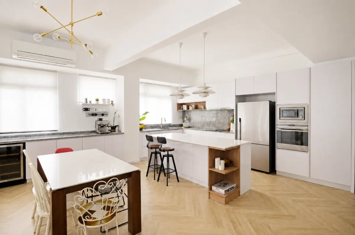 Bright, modern white kitchen with island, stainless steel appliances, and a wooden dining table with chairs on a herringbone floor