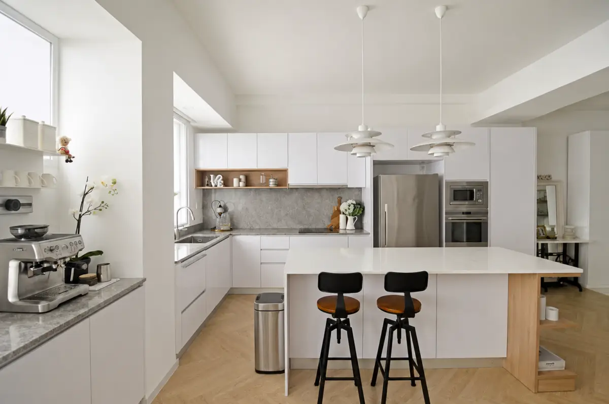 Bright modern kitchen with white cabinets, marble island, and two black-and-wood bar stools in front of a spacious island.