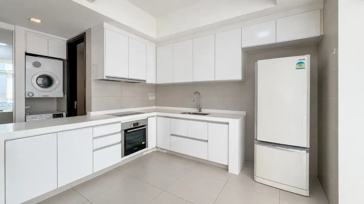 Modern all-white kitchen with an L-shaped counter, built-in oven, induction hob, sink, and a tall fridge.