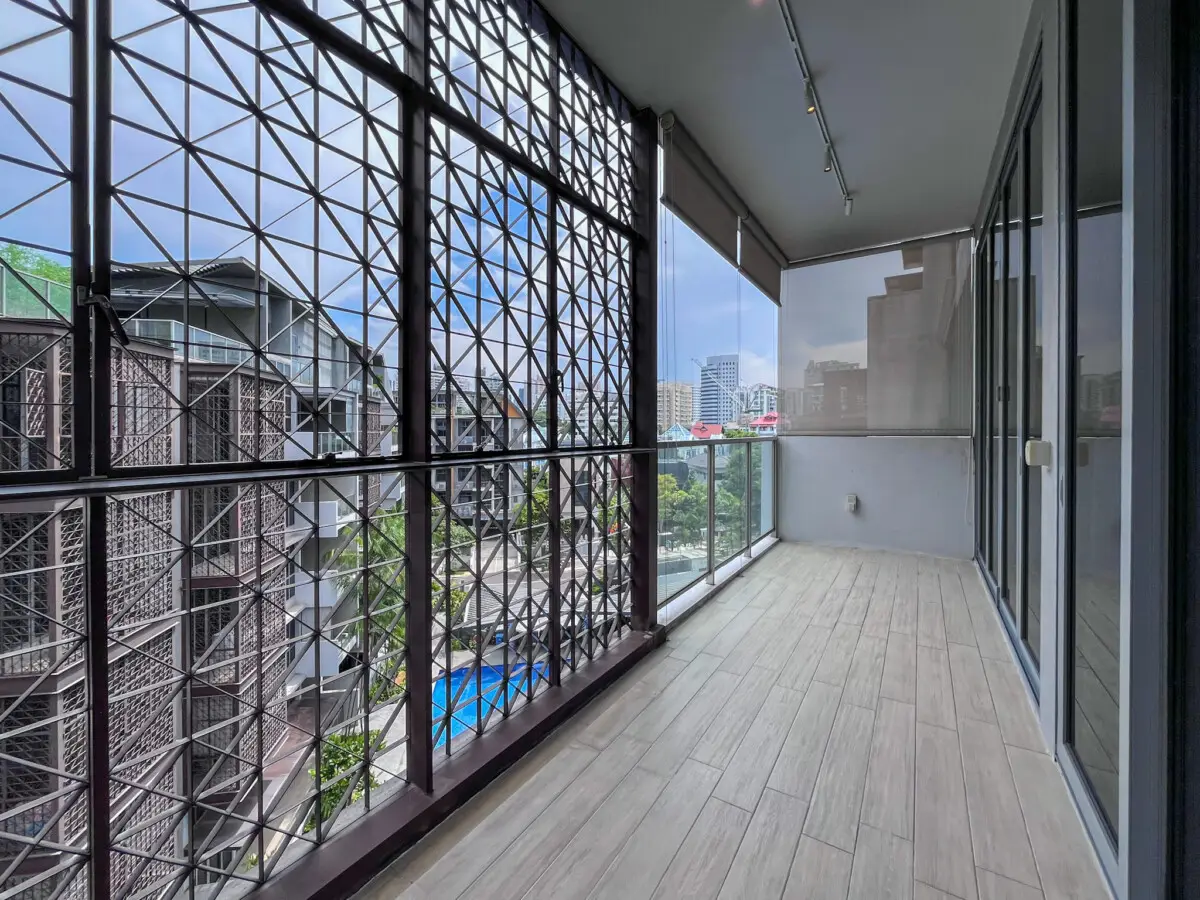 Balcony with a metal lattice railing and glass barrier overlooking a city skyline.
