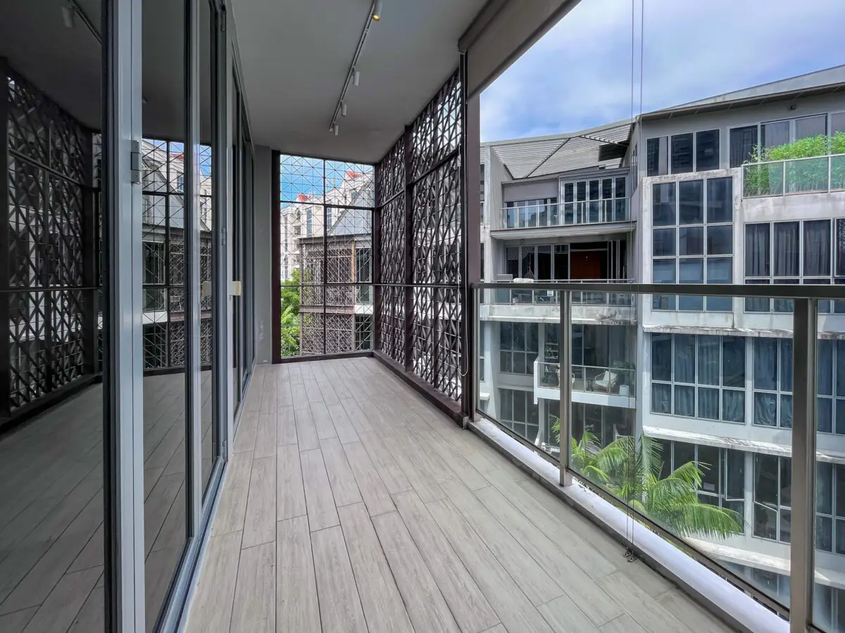 Balcony with light wood-like tiles, glass railing, and a view of modern apartment buildings across the way.