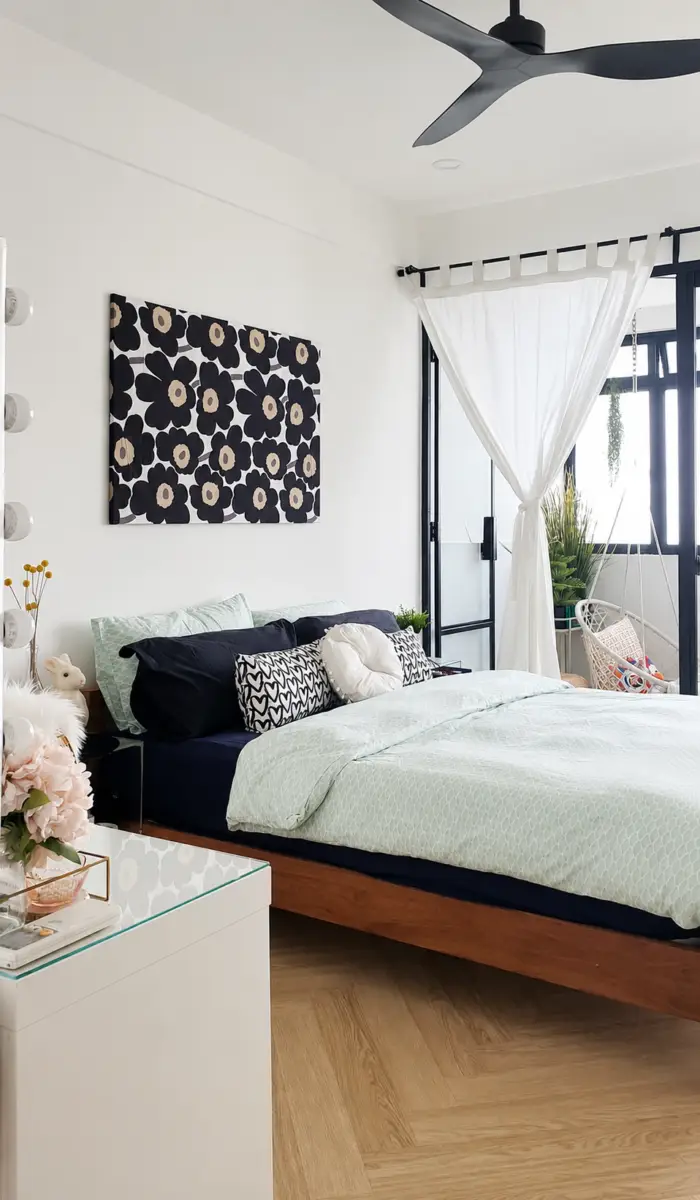 Bedroom with mint-green bedding and navy pillows, a black floral canvas above the bed, and a glass-topped nightstand with flowers.