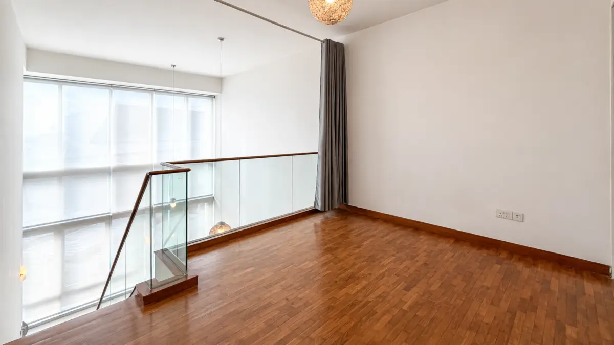 Empty loft area with wooden flooring, glass balustrade, and large windows letting in daylight.
