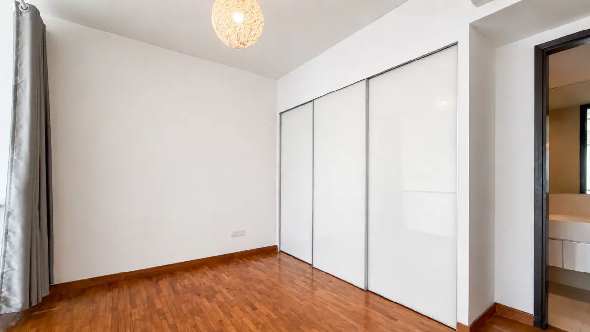 Empty modern bedroom with white walls, dark wood floor, a round woven pendant light, grey curtains on the left, and frosted glass sliding doors for a built-in wardrobe on the right.