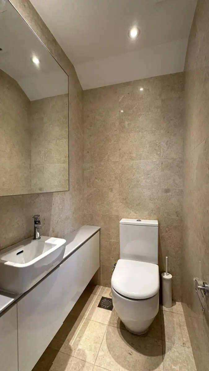 Modern beige-tiled bathroom with white sink, wall cabinet, and large mirror above a floating vanity.