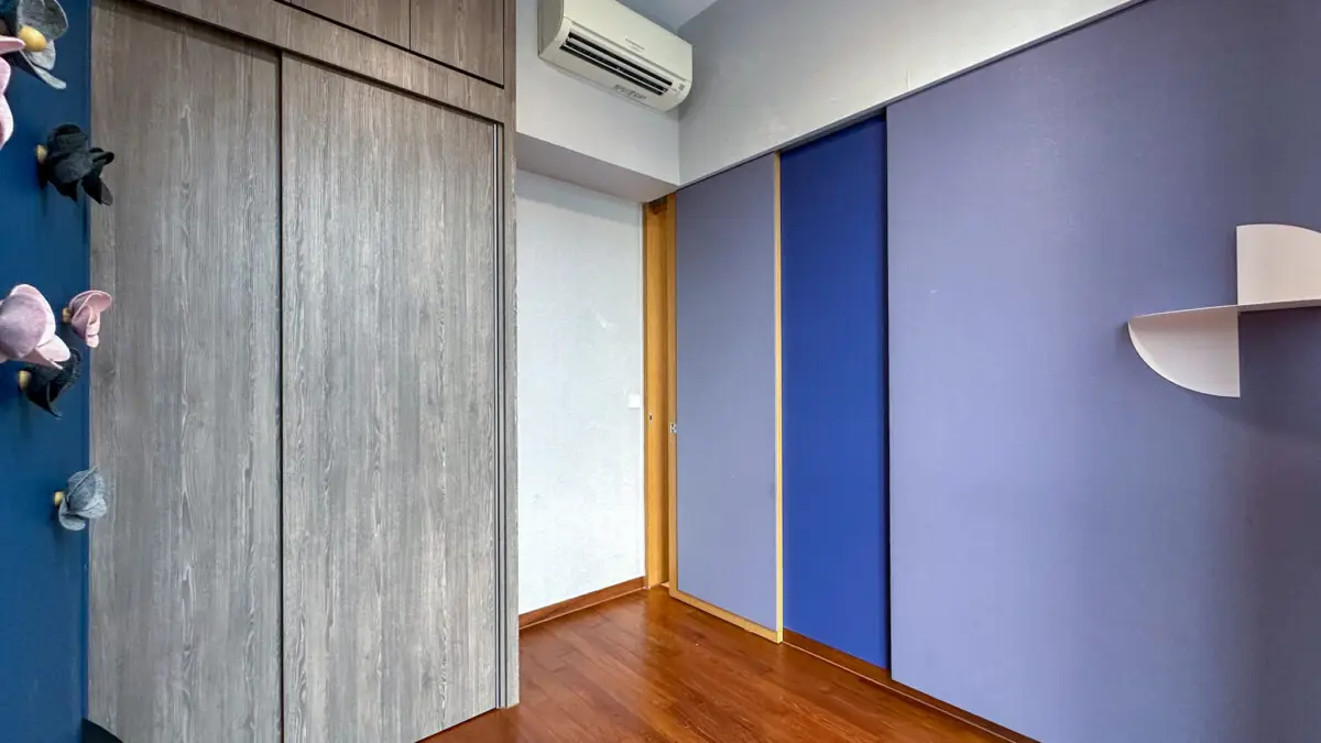 Corner of a room with gray wood wardrobe doors, blue and purple wall panels, a curved white shelf, and a wood floor.