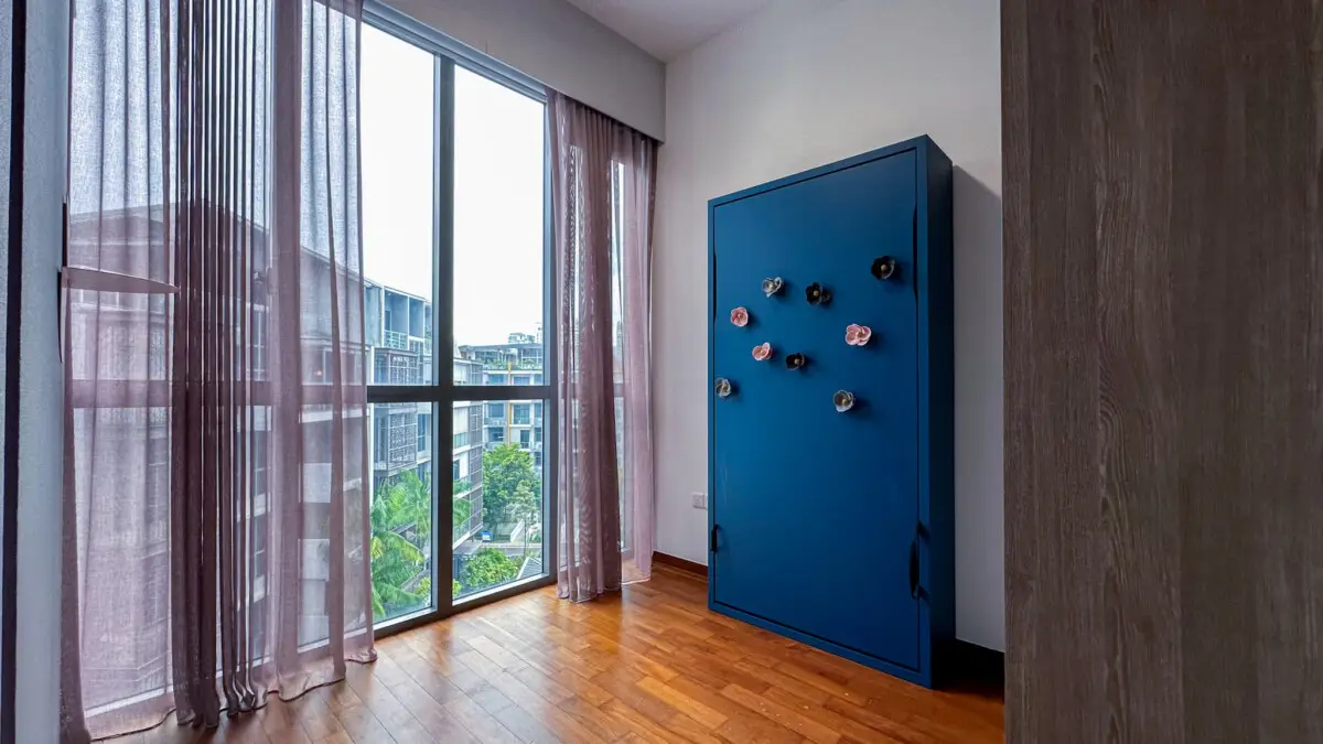 Room with tall windows and sheer purple curtains; a blue upright wardrobe with decorative flower magnets on the right, and a wooden floor nearby.