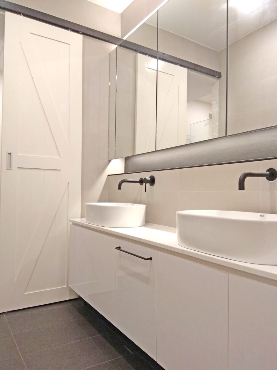 Modern bathroom with double pedestal sinks, white cabinetry, and a large mirrored wall.