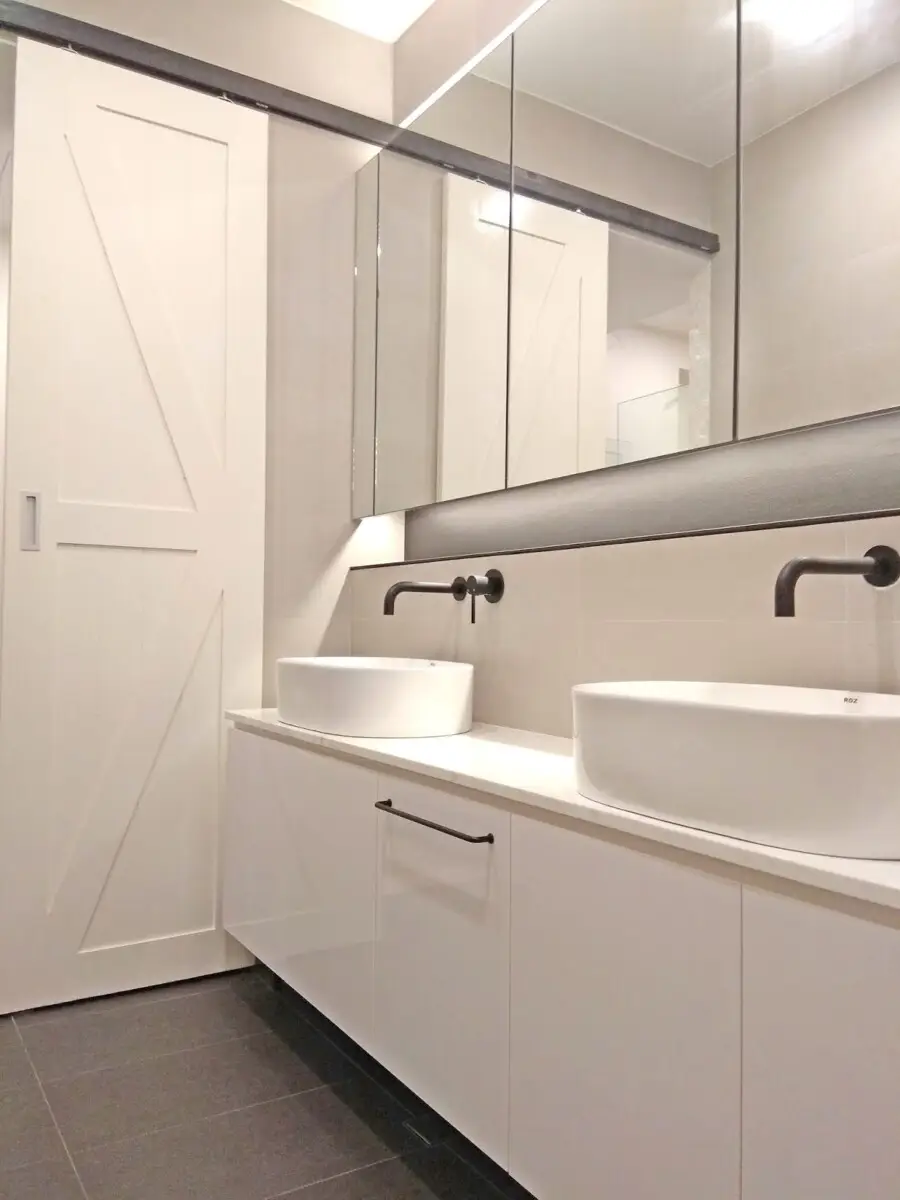 Modern bathroom with double pedestal sinks, white cabinetry, and a large mirrored wall.