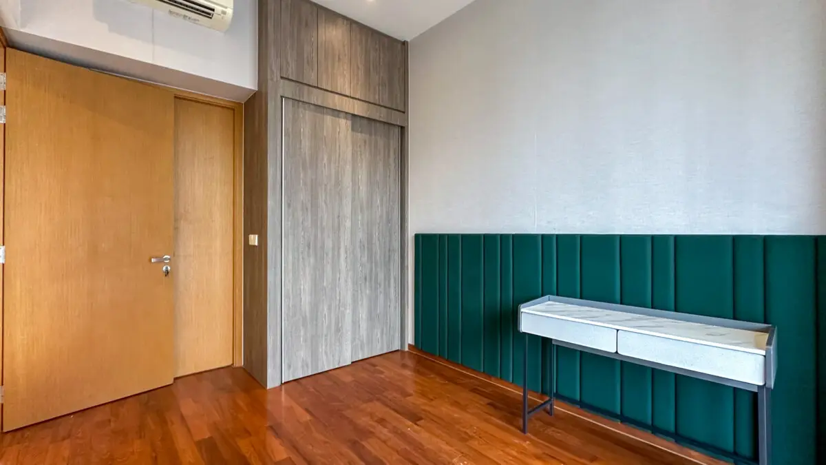 Interior room corner with a wooden door on the left, gray wood closet, and teal padded wall below; a narrow gray two-drawer console rests against the teal panels.