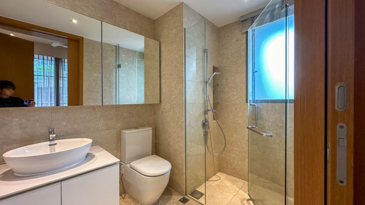 Modern bathroom with beige tiled walls, glass shower enclosure, white toilet, and a white oval vessel sink on a sleek vanity.