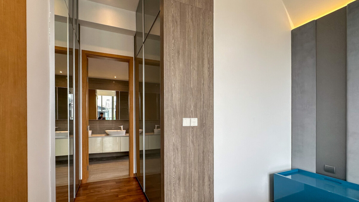 Modern bathroom suite view: vanity with sinks visible through a wooden-framed doorway and mirrored panels along a hallway.