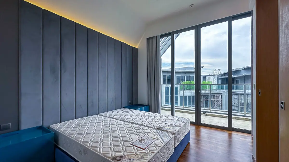 Bedroom with two twin beds on blue frames, a gray padded wall, and a large glass door to a balcony.
