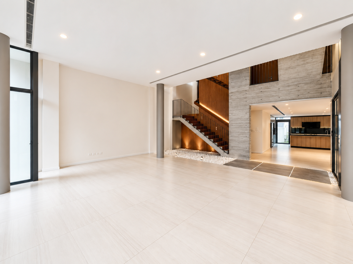 Spacious modern living area with large light tiles, a wooden staircase, and open-plan kitchen in the background.