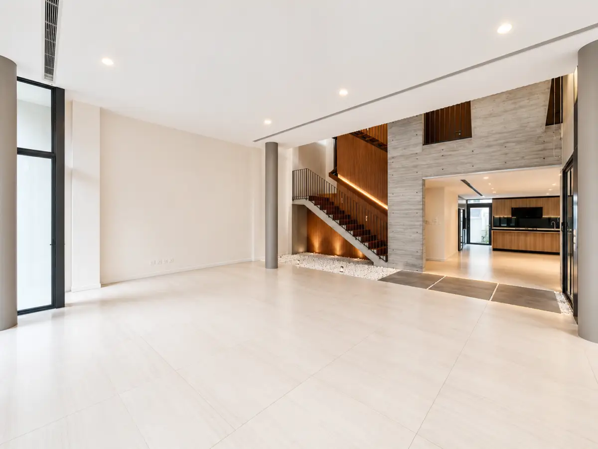 Spacious modern living area with large light tiles, a wooden staircase, and open-plan kitchen in the background.