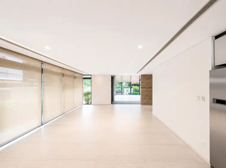 Interior modern lobby with large beige roller blinds along left wall and glass doors at the far end; bright, minimalist space with light tiled floor and white walls