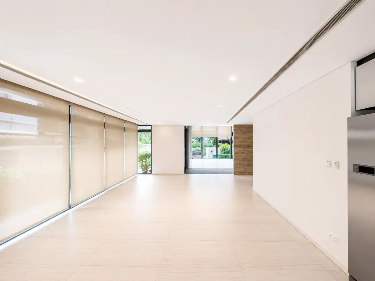 Interior modern lobby with large beige roller blinds along left wall and glass doors at the far end; bright, minimalist space with light tiled floor and white walls