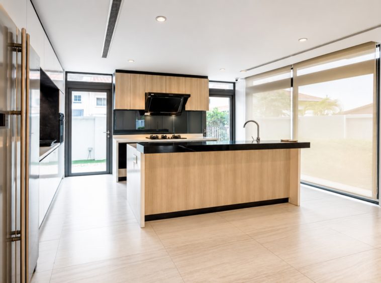 Modern kitchen with a large wood island, black countertop, stainless fridge, and gas cooktop under a range hood; bright, airy space with glass doors to the yard.