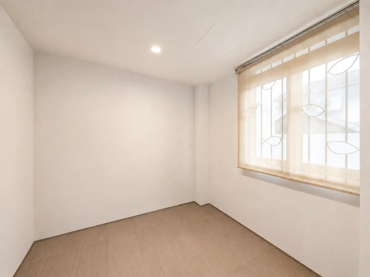 Empty white-walled room with beige tiled floor and a large window covered by sheer blinds letting in soft light