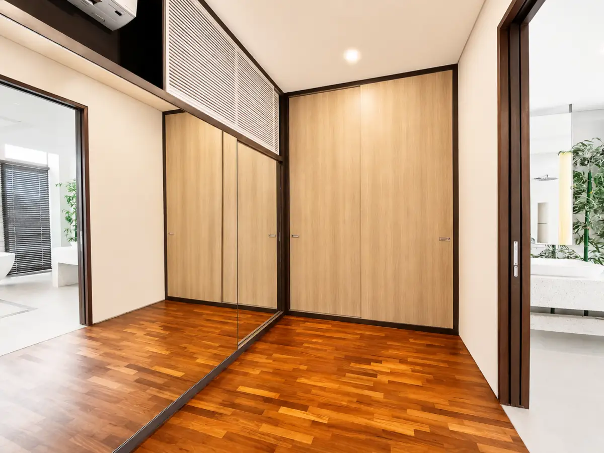 Hallway with warm parquet floor, tall wooden closets, and a large mirrored wall on the left.