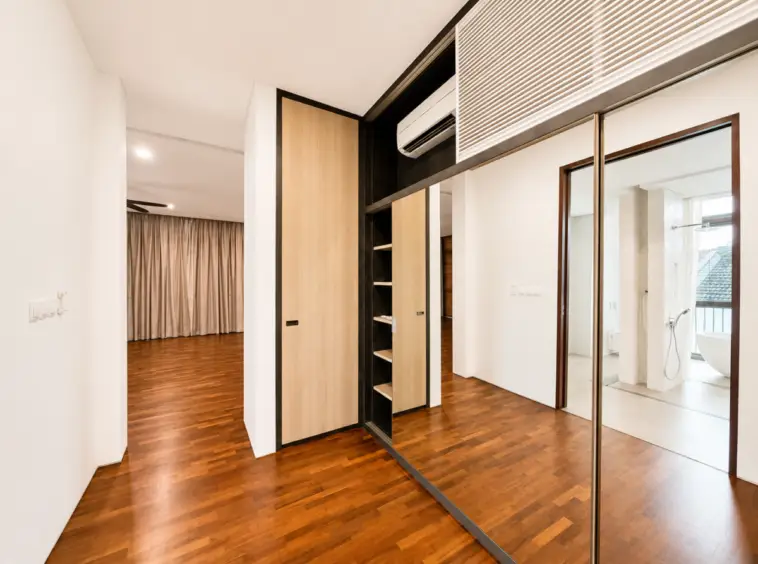 Modern hallway with wooden floors, built-in wardrobe with shelves and mirrored sliding doors, leading to a bathroom area.
