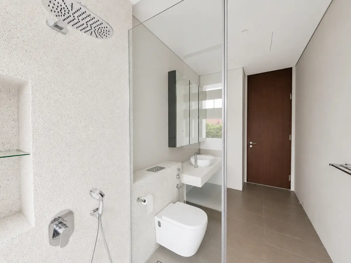Modern bathroom with a glass shower partition, wall-hung toilet, and stone countertop sink opposite a wooden entry door.