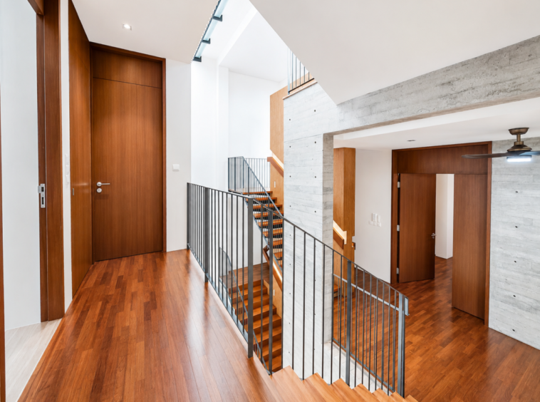 Bright modern interior hallway with warm wooden floors, wooden doors, and a black metal railing along a staircase.
