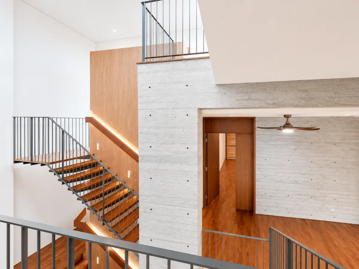 Open multi-level atrium with wooden floors, concrete walls, and metal railings; a staircase winds between levels.