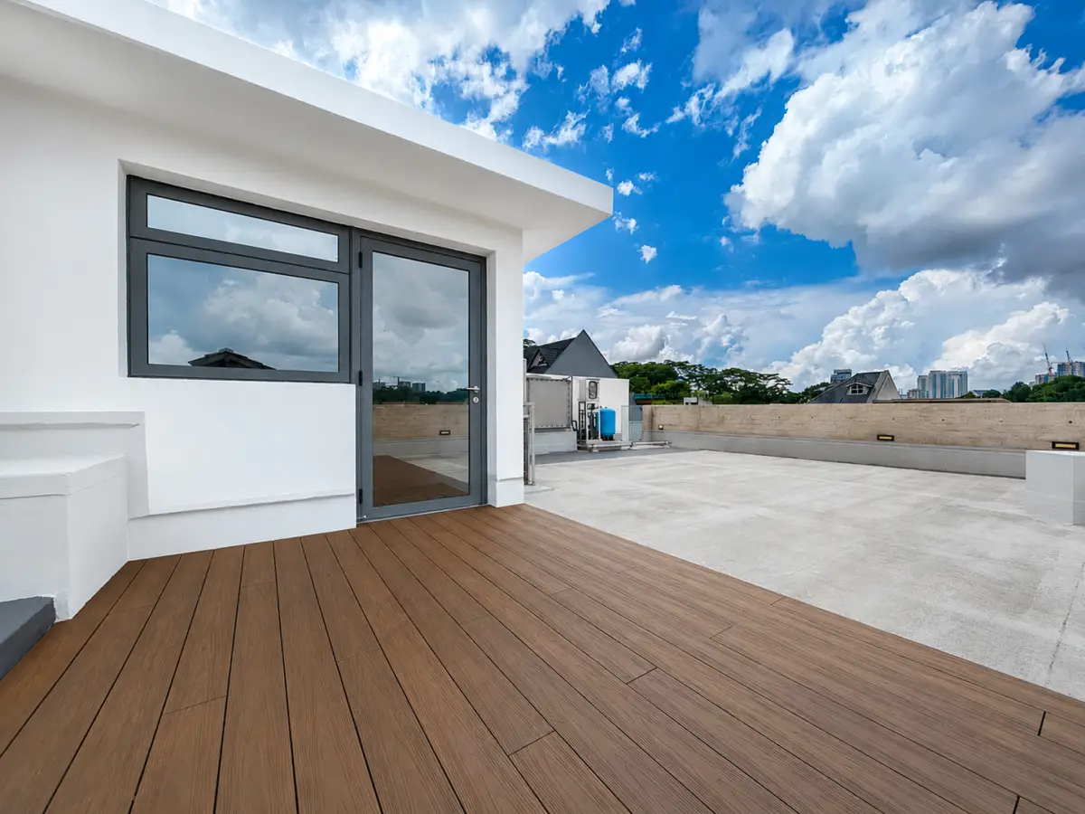 Rooftop terrace with a glass door, white walls, and a brown wooden deck under a blue sky.