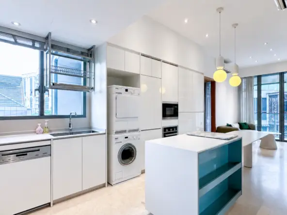 Open-plan modern kitchen with white cabinetry, large island, and stacked laundry appliances beside tall pantry cabinets.