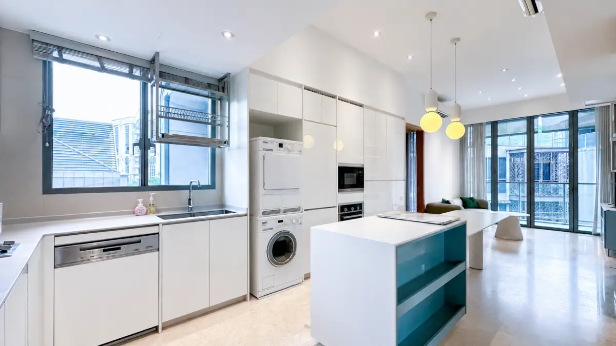 Open-plan modern kitchen with white cabinetry, large island, and stacked laundry appliances beside tall pantry cabinets.