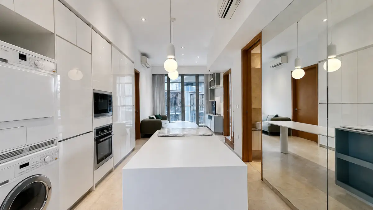 Open-plan kitchen with white high-gloss cabinets, built-in oven and microwave, and a central white island; living room with a green sofa visible at the back.
