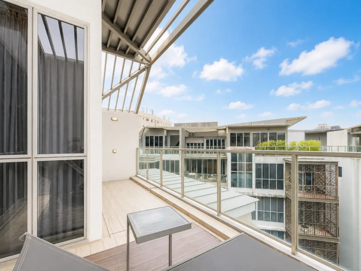 Balcony with glass railing overlooking a modern white apartment complex under a blue, partly cloudy sky.