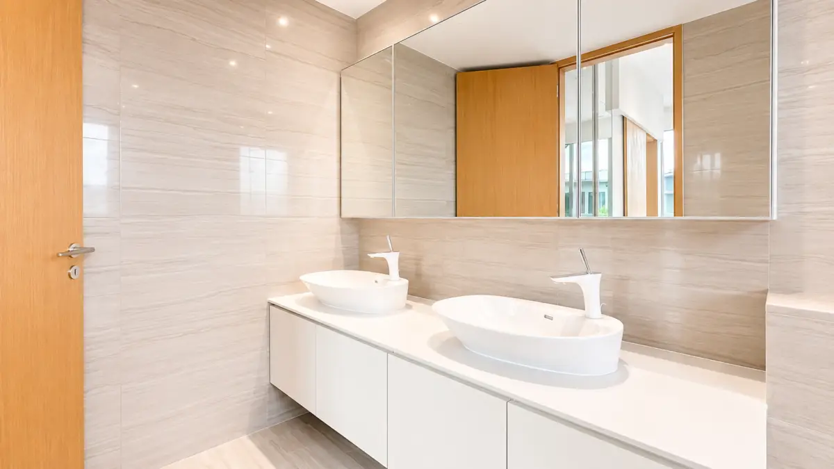 Modern bathroom with two white vessel sinks on a white countertop, mirrored cabinet above, and a wooden door on the left.