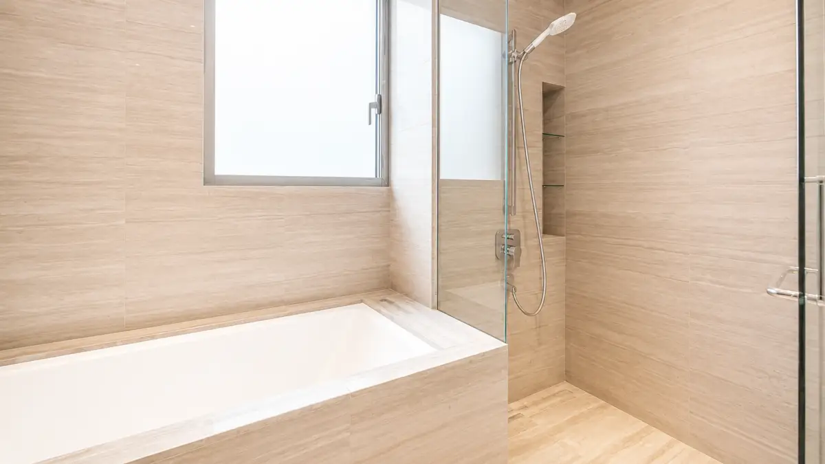 Beige tiled bathroom with a built-in white bathtub and glass-enclosed shower area.