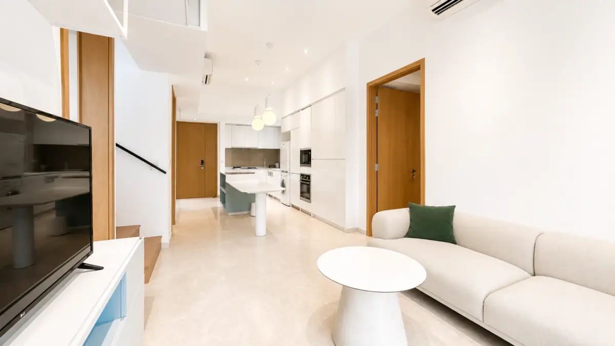 Open-concept living area with a beige sofa, white coffee table, and a modern kitchen in the background.
