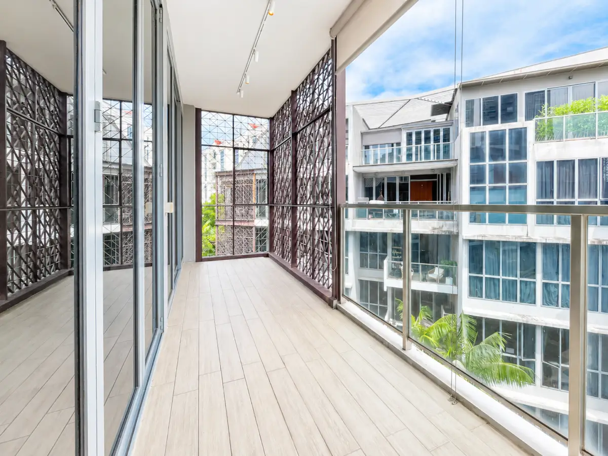 Balcony walkway with glass sliding doors on left and a glass railing overlooking neighboring modern buildings.