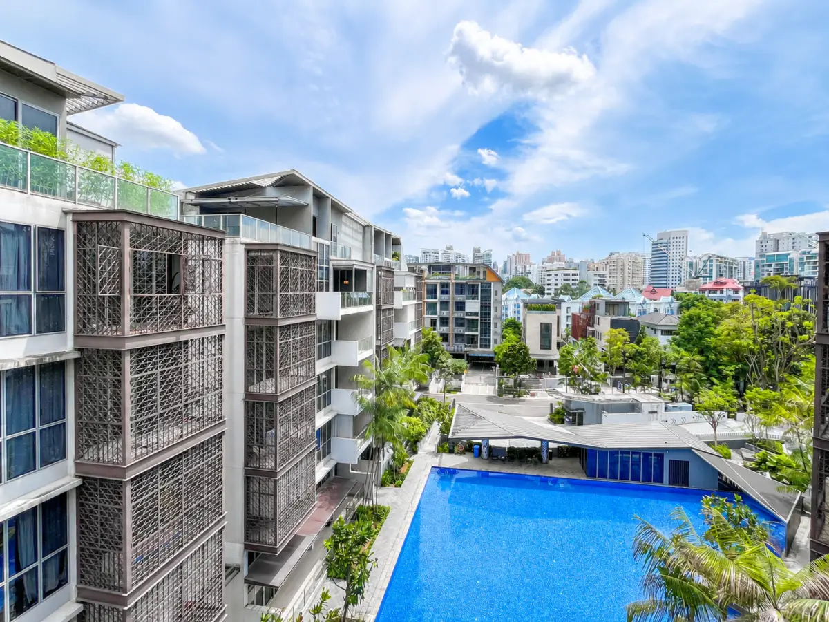Modern apartment complex with a large blue swimming pool and palm trees, under a bright blue sky.