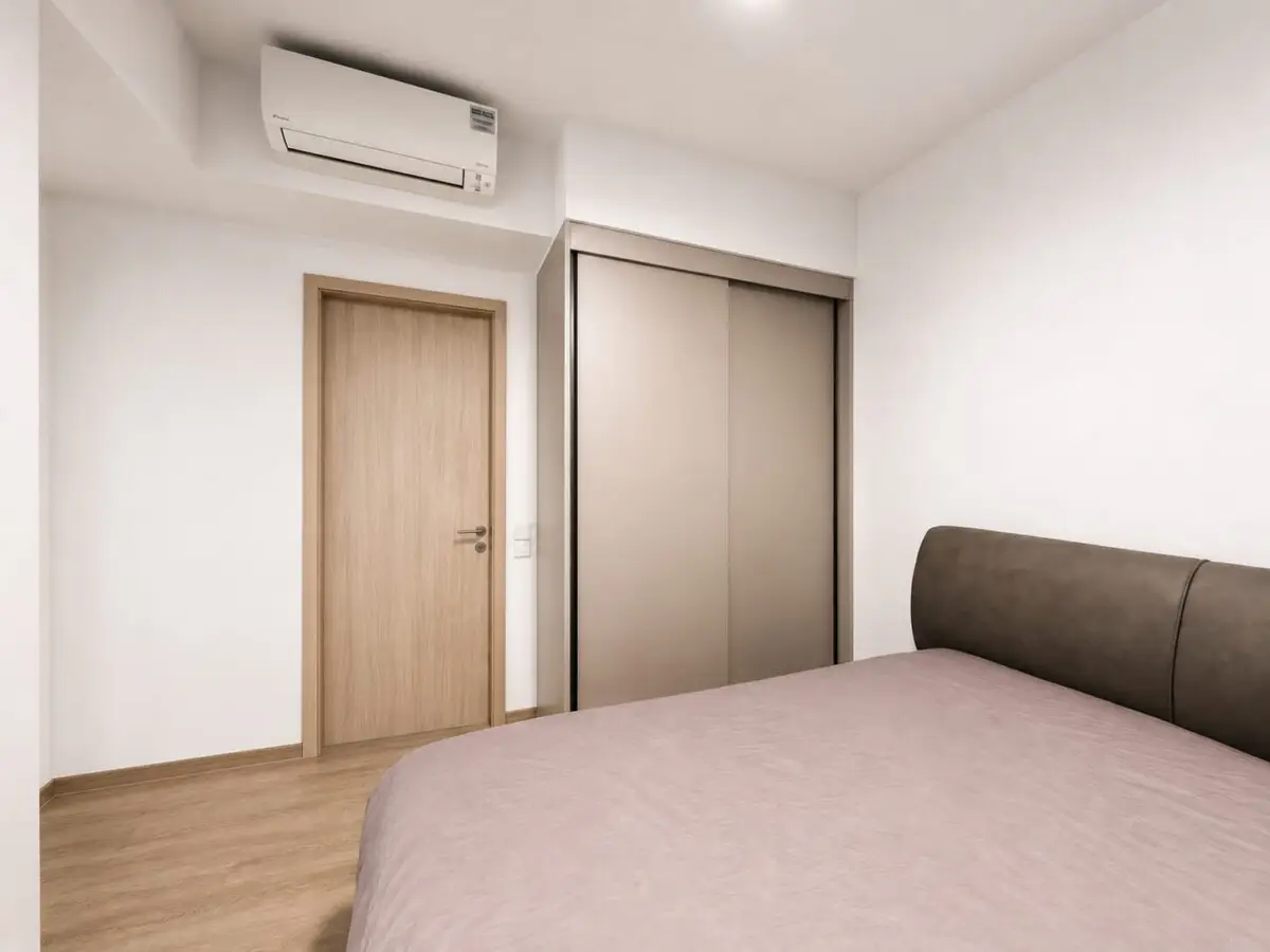 Minimalist bedroom with a beige bedspread and brown upholstered headboard, wooden floor, a wooden door, and a beige sliding wardrobe.