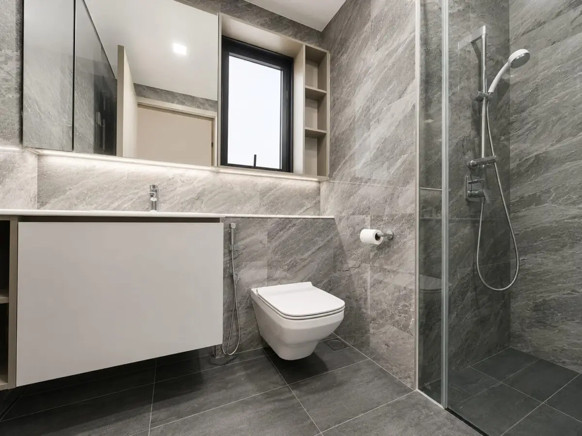 Modern gray marble bathroom with glass shower enclosure, wall-mounted vanity, and wall-hung toilet.
