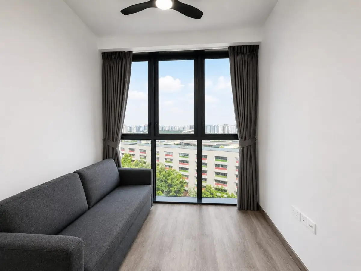 Living room with a gray sofa facing a large window, dark curtains pulled to the sides, overlooking a cityscape under a blue sky.